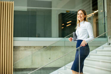 Cute young business woman walking on stairs in the office hallway - INGF13108