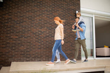 Family with a mother, father, son and daughter walking by the wall of a brick house - INGF13133