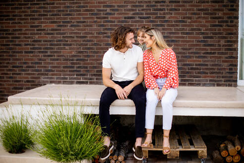 Family with a mother, father and daughter sitting outside on steps of a front porch of a brick house - INGF13137