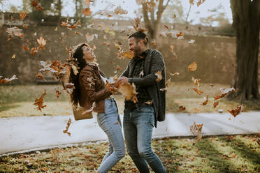 Handsome young couple having fun with leaves in autumn park - INGF13146