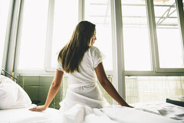 Young woman sits on a bed with white linen - INGF13154