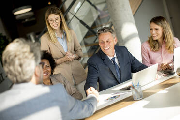 Business people shaking hands while sitting by the desk in the office - INGF13176