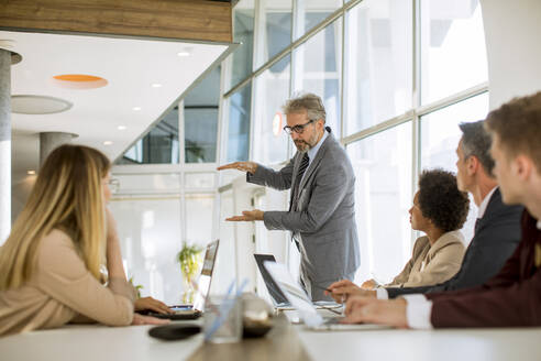 Mature businessman explaining strategy to group of multiethnic business people while working on new project in the office - INGF13179