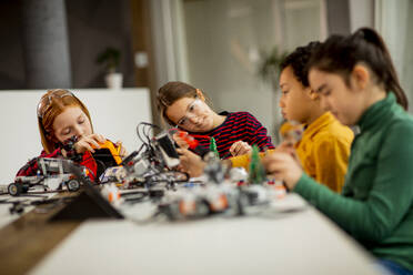 Group of happy kids programming electric toys and robots at robotics classroom - INGF13212