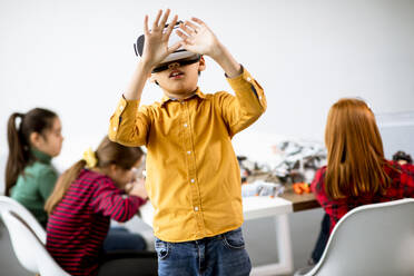 Cute little boy wearing VR virtual reality glasses in a robotics classroom - INGF13214