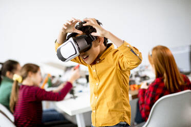 Cute little boy wearing VR virtual reality glasses in a robotics classroom - INGF13215