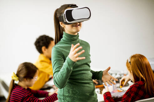 Cute little girl wearing VR virtual reality glasses in a robotics classroom - INGF13217