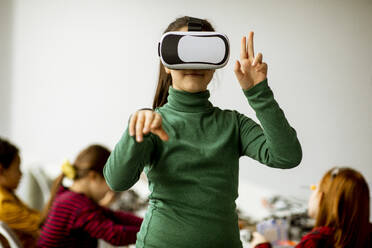 Cute little girl wearing VR virtual reality glasses in a robotics classroom - INGF13218