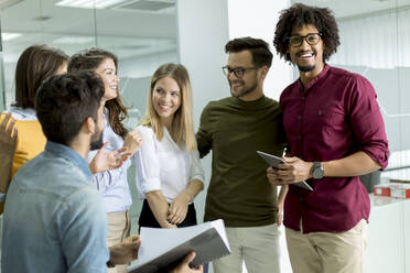 Multiethnic group of young people standing in modern office and brainstorming - INGF13230