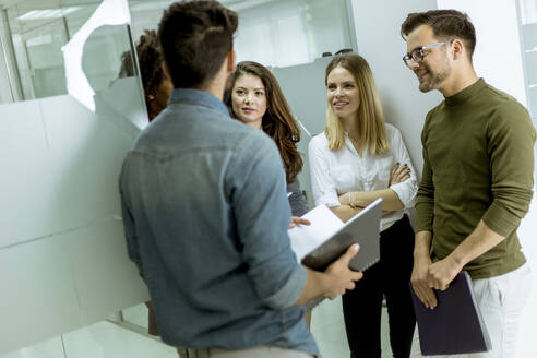 Multiethnic group of young people standing in modern office and brainstorming - INGF13232