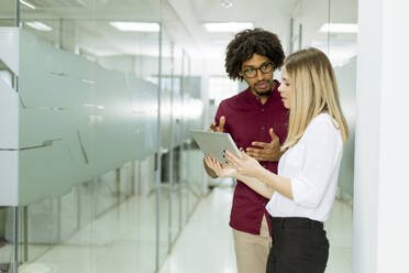 Young African american businessman and caucasian businesswoman with tablet pc computer standing in office - INGF13240