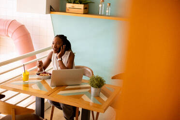 Pretty young black woman having a healthy breakfast while working on laptop in the cafe - INGF13269