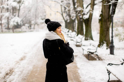 Pretty young woman in warm clothes enjoying in snow with takeaway coffee cup - INGF13271