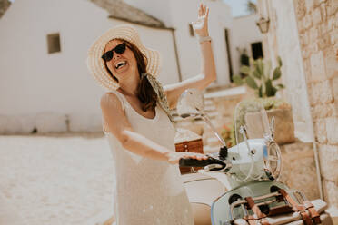 A young woman in a white dress and hat on a sunny day during tourist visit in Alborebello, Italy - INGF13273