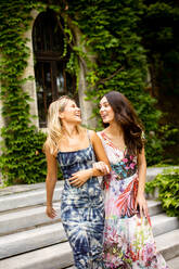 Two pretty young women walking by the old house with ivy - INGF13277