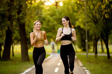 Two pretty young women running on a lane in the park - INGF13279