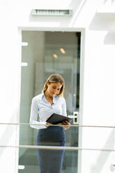 Young business woman with digital tablet standing in the modern office wallway - INGF13295