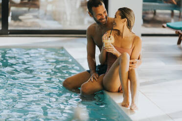 Handsome young couple relaxing by the indoor swimming pool - INGF13306