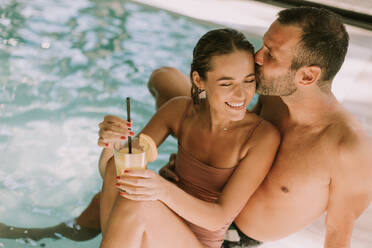 Handsome young couple relaxing by the indoor swimming pool - INGF13307