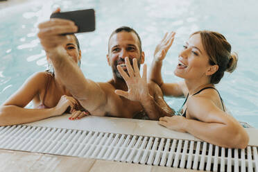 Handsome young people relaxing in the indoor swimming pool and taking selfie with mobile phone - INGF13308