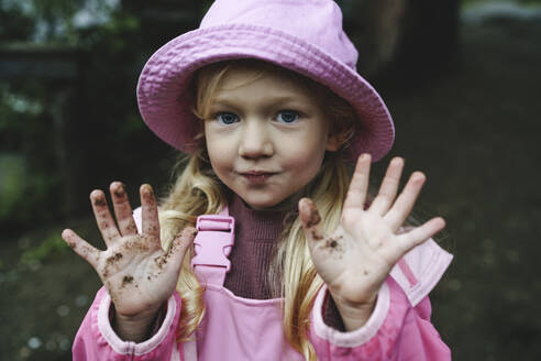 Girl in pink raincoat and hat showing dirty hands - NSTF00026