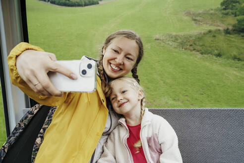 Glückliche Frau nimmt Selfie mit Tochter durch Handy in Skilift - NSTF00028