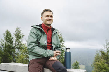 Happy man sitting with insulated drink container - NSTF00040