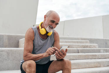 Smiling senior man using smart phone sitting on staircase - OIPF04044