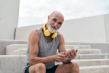 Smiling retired senior man using smart phone sitting on staircase - OIPF04046