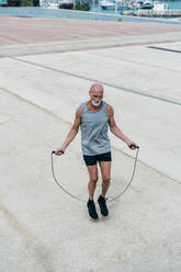 Aktiver älterer Mann, der auf dem Gehweg mit einem Springseil trainiert - OIPF04053