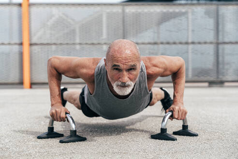 Entschlossener älterer Mann bei einer Plank-Übung an Griffen - OIPF04057