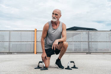 Active senior man kneeling by handles on footpath - OIPF04059