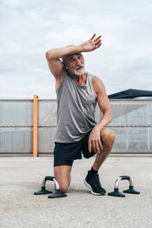 Tired senior man kneeling by handles on footpath - OIPF04060