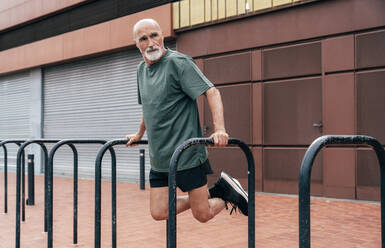 Aktiver älterer Mann beim Training am Barren vor einem Gebäude - OIPF04085