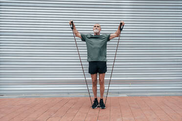 Aktiver älterer Mann, der mit einem Aufhängegurt vor einem Rollladen trainiert - OIPF04091