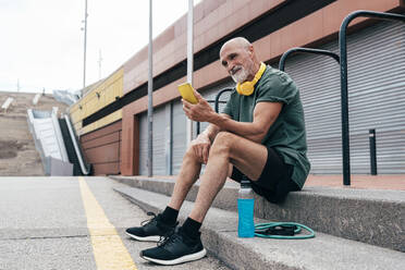Smiling senior man using smart phone sitting on steps - OIPF04092