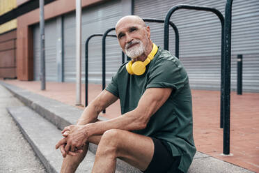 Senior man with wireless headphones sitting on steps - OIPF04093
