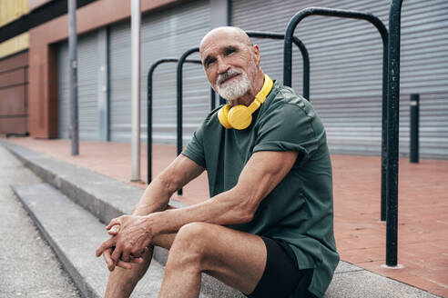 Senior man with wireless headphones sitting on steps - OIPF04093