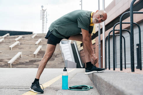 Retired senior man tying shoelace by parallel bars - OIPF04095