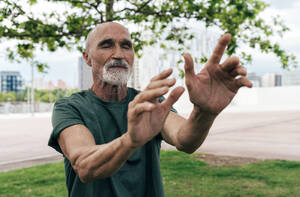Aktiver älterer Mann, der mit geschlossenen Augen im Park trainiert - OIPF04104