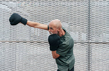 Retired senior man practicing with boxing gloves by fence - OIPF04109