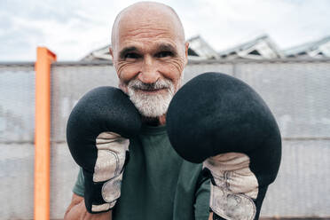 Smiling senior man practicing with boxing gloves - OIPF04111