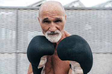 Confident shirtless senior man practicing with boxing gloves - OIPF04113