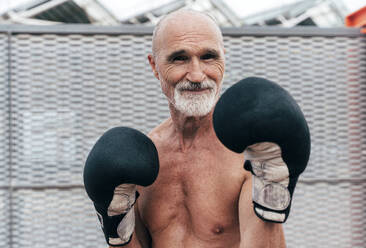 Smiling shirtless senior man practicing with boxing gloves - OIPF04115