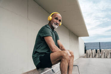 Senior man listening to music through wireless headphones sitting on bench - OIPF04119