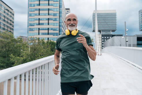 Smiling active senior man running on footbridge - OIPF04123