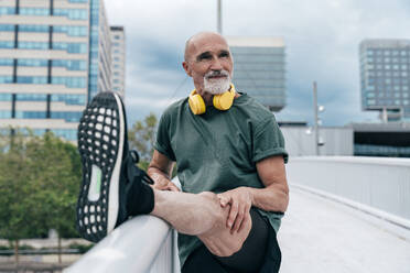 Retired senior man stretching leg on railing at footbridge in city - OIPF04126