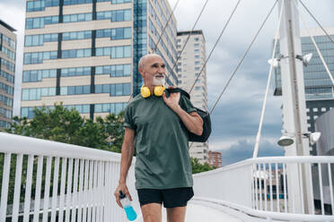 Aktiver älterer Mann mit Energydrinkflasche und Tasche auf einer Fußgängerbrücke - OIPF04130