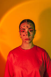 Young woman with gemstones on face in neon lighting against orange background - EGHF00862