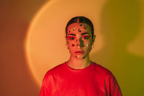 Junge Frau mit Edelsteinen im Gesicht bei Neonbeleuchtung im Hintergrund - EGHF00863
